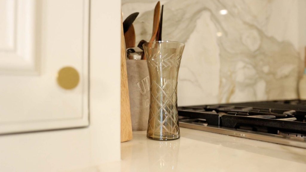 To add warm tones into her kitchen for fall, Amitha Verma places a smoky glass vase with etched details next to her stove. A simple way to start late summer early fall decorating.